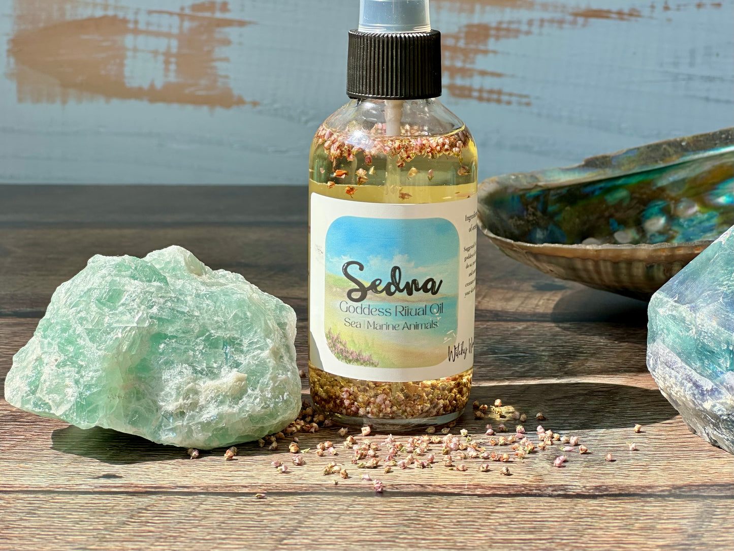 Bottle of Sedna Goddess Ritual oil with a label on a wooden surface with rocks and a shell.