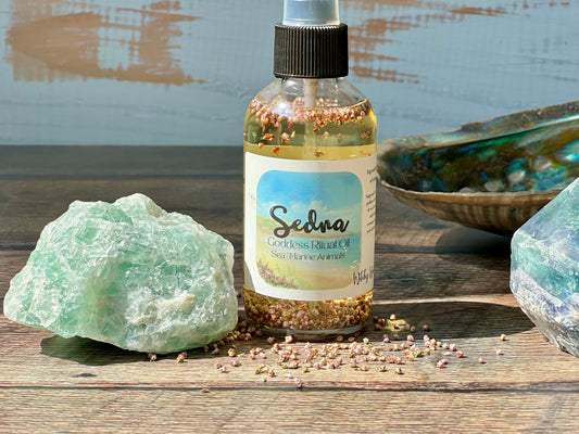 Bottle of Sedna Goddess Ritual oil with a label on a wooden surface with rocks and a shell.