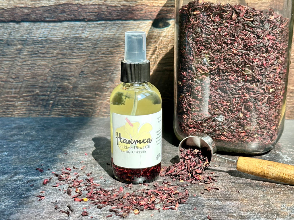 Bottle of 'Haumea' Goddess Ritual Oil with dried herbs on a wooden surface