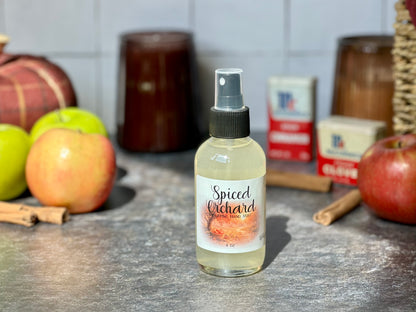 Spiced Orchard Purifying Hand Mist bottle on a countertop with apples and cinnamon sticks in the background.