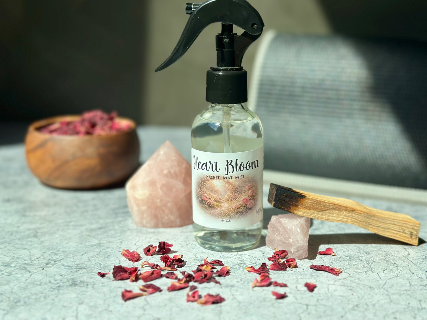Heart Bloom Sacred Mat Mist bottle with pink crystals and dried rose petals on a textured surface.