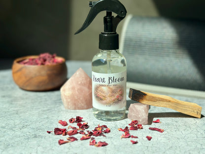 Heart Bloom Sacred Mat Mist bottle with pink crystals and dried rose petals on a textured surface.